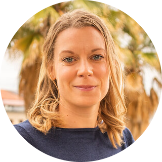 A headshot of Lisa Rennels looking at the camera, in front of palm trees on the Stanford campus.